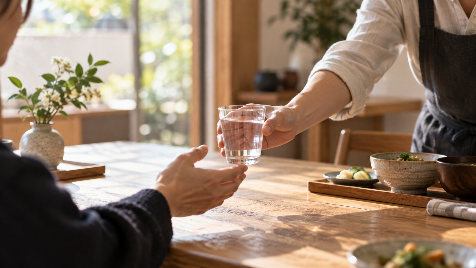 One adult offers another a glass of water across a wooden table.